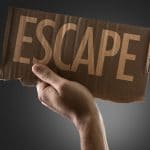 An individual holding up a piece of cardboard with the word Escape written on it