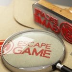 escape game written with a stamp on a tan colored piece of parchment with a magnifying glass over it